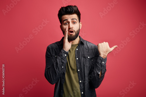 awesome guy with a palm on his mouth, gossiping, whispering something to the camera. close up photo. guy telling a secret. chatterbox