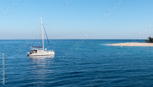 Sailing boat at anchor in front of a small tropical island resort