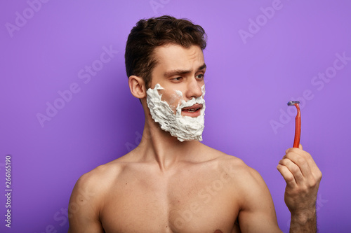 attractive awesome man with foam on his face looking at the desposable razor. close up photo photo