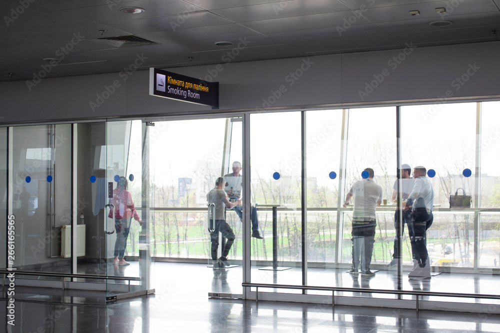 People in smoking room at international airport. Smoking sign on english and ukrainian.