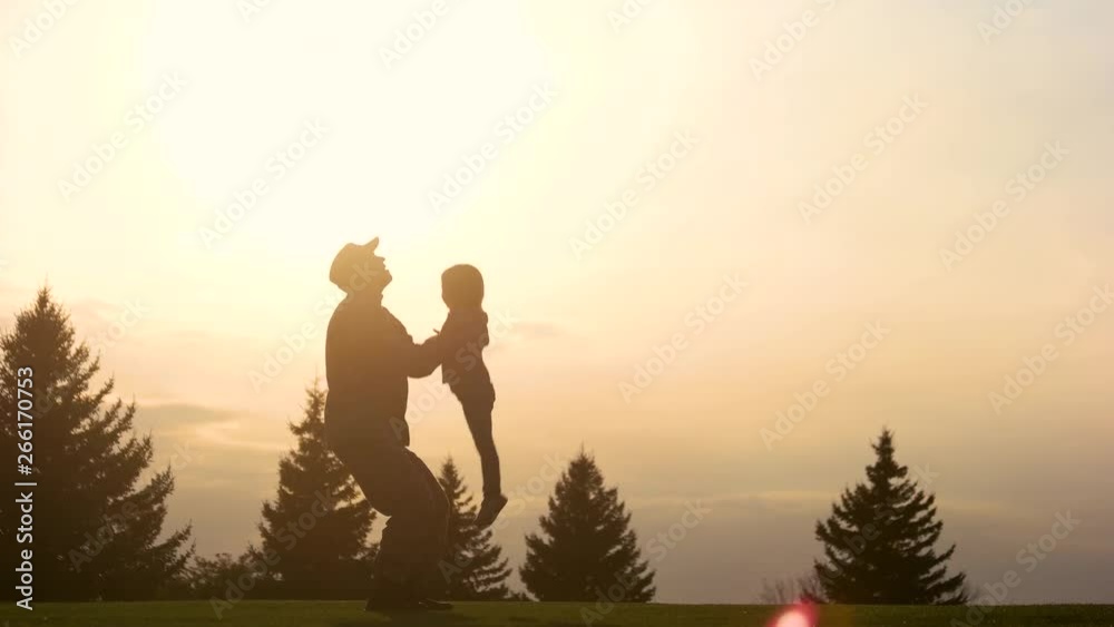 Playing with daughter in the evening park. Silhouette of military father lifting up and down little girl into the air. Playing with daughter in the evening park. Silhouette of military father lifting up and down little girl into the air.
