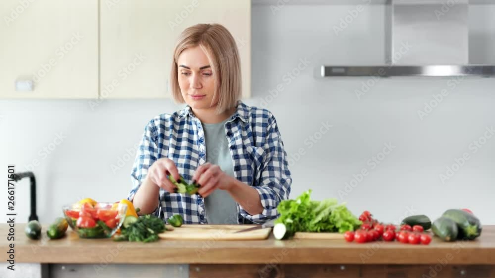 Beautiful vegan woman cooking fresh salad and trying vegetables looking at camera medium shot Beautiful vegan woman cooking fresh salad and trying vegetables looking at camera medium shot