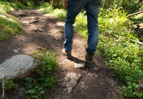 Man visible from the waist down hiking along a trail surrounded by lush greens