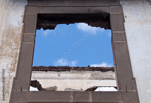 empty window frame in a roofless abandoned house with white interior walls against a blue sky