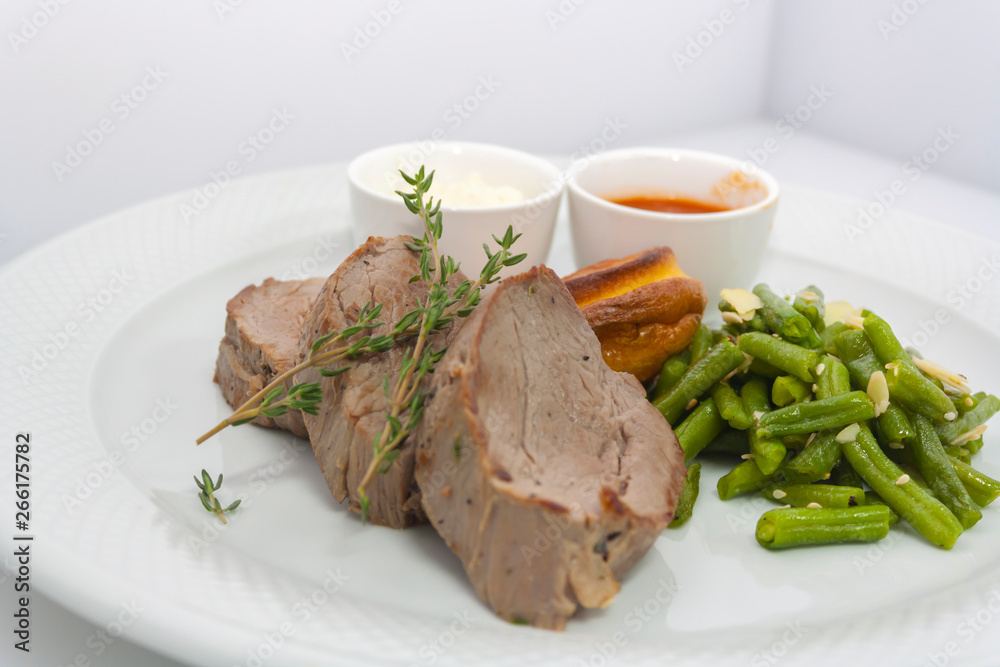 roast beef and yorkshire pudding with baked green beans on white background