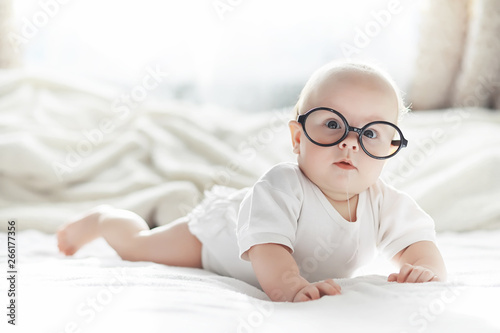 A newborn baby is lying on a soft bed in glasses.