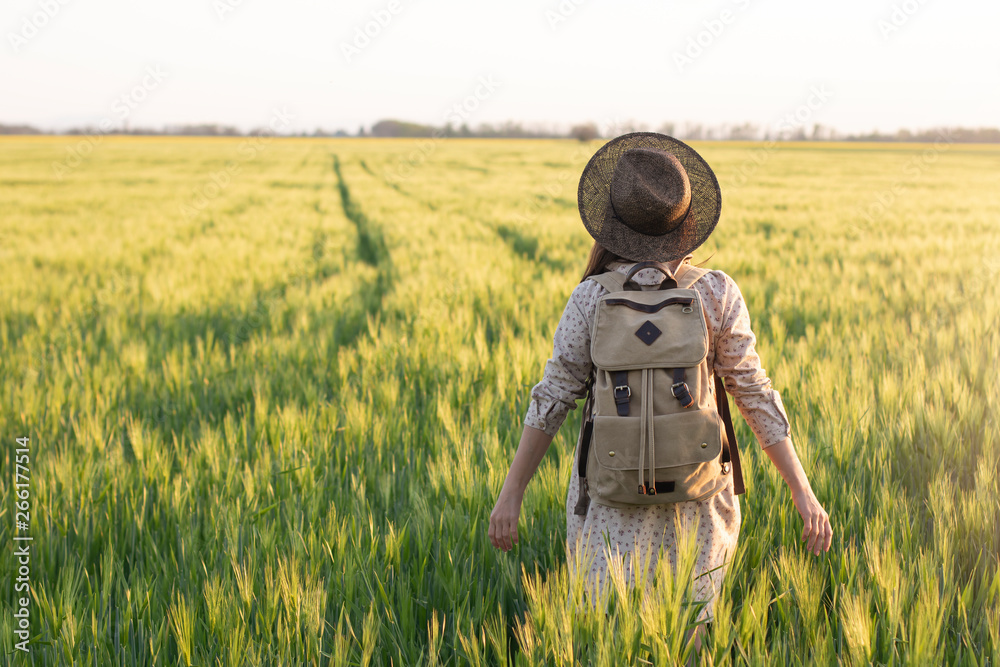 Traveler with a backpack in a field of wheat. Happy woman outdoors in nature with her arms open. The concept of freedom and discovery. Environment and lifestyle