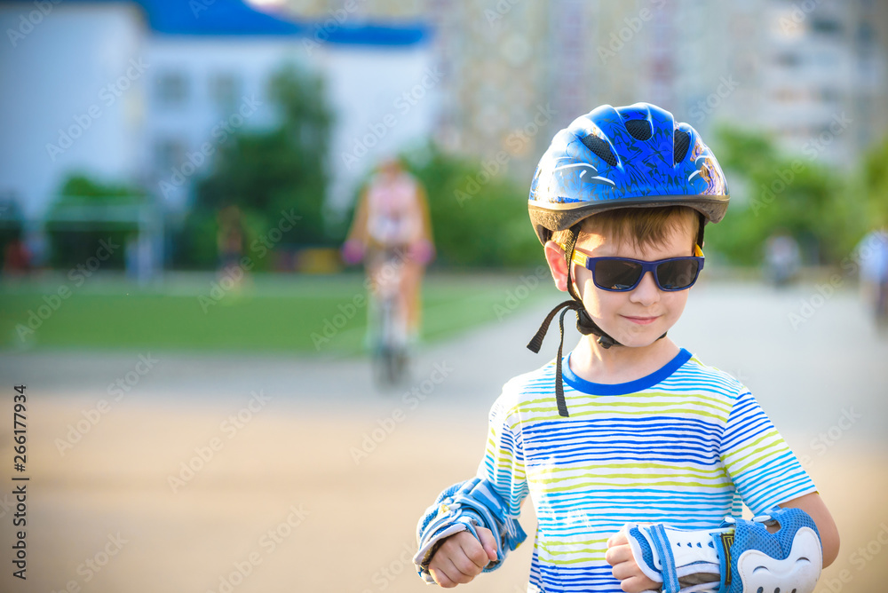 Little boy riding on rollers in the summer in the Park. Happy child in helmet learning to skate. Safety in sport