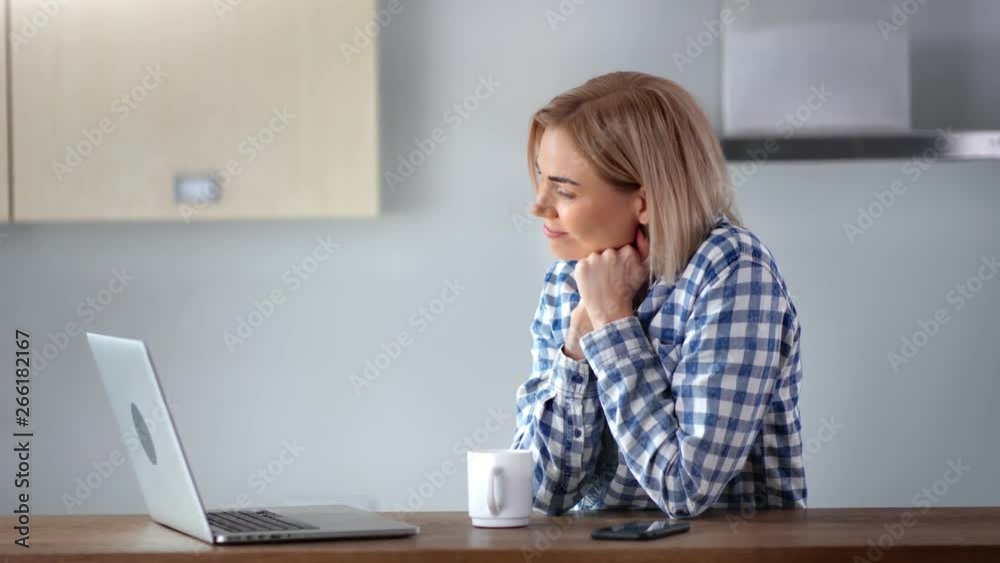 Smiling young domestic woman using laptop pc at home kitchen enjoying weekend medium close-up Smiling young domestic woman using laptop pc at home kitchen enjoying weekend medium close-up