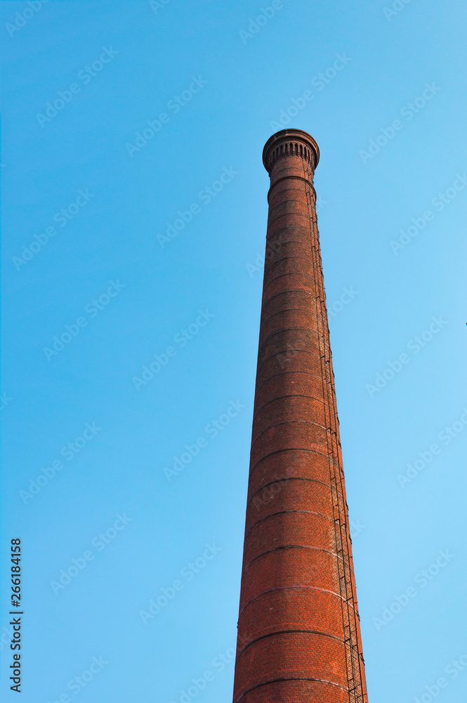 Red brick factory pipe against blue sky. The concept of environmental pollution by harmful emissions into the atmosphere.
