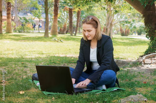 Young girl freelancer works with a laptop outdoors in the park. The concept of freelance work of the manager, remote business management