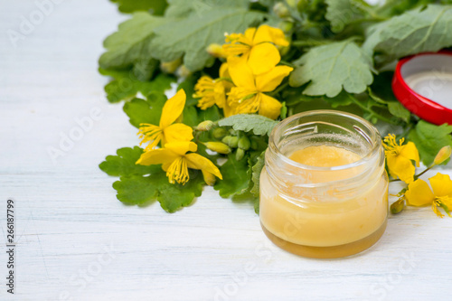 A small glass jar of dermatological ointment on the basis of the herb celandine on a wooden background. Selective focus.