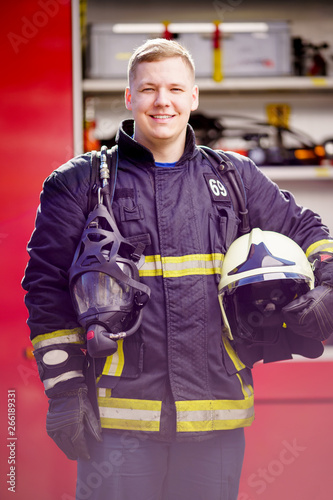 Photo of happy man firefighter with helmet in his hands against background of fire truck