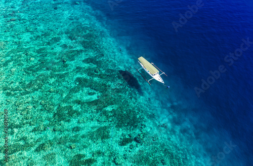 Boat on the water surface from top view. Turquoise water background from top view. Summer seascape from air. Gili Meno island, Indonesia. Travel - image © biletskiyevgeniy.com