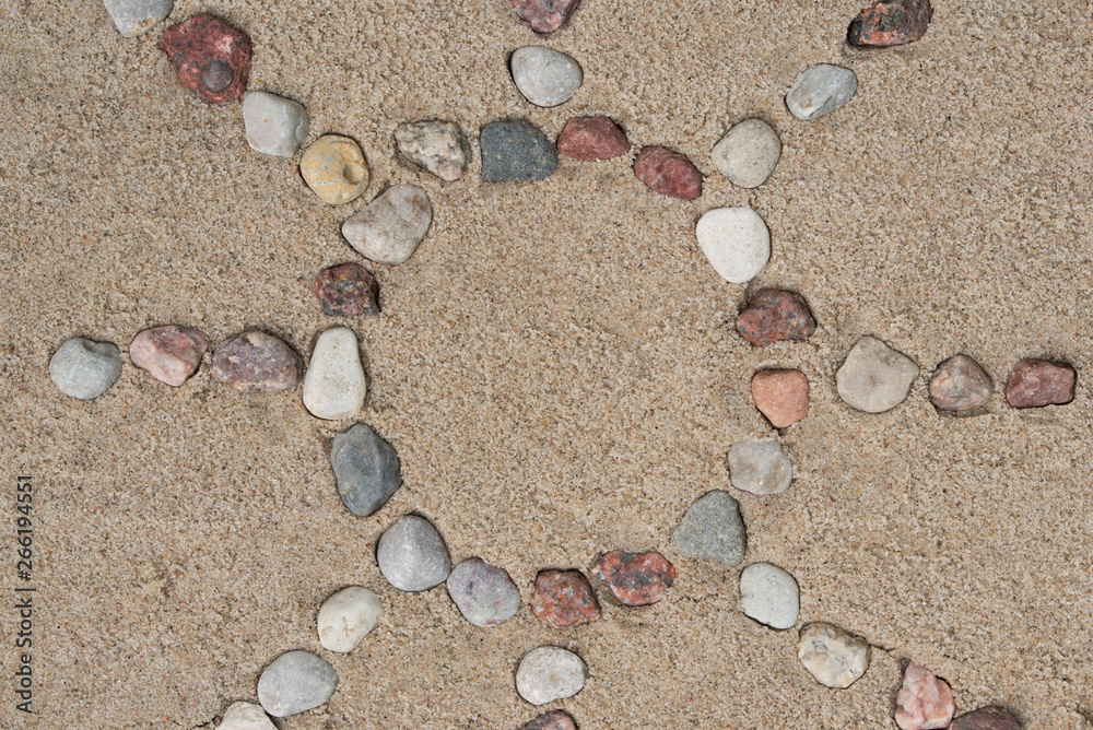 sun shape made of pebble stones on sand background sun shape made of pebble stones on sand background