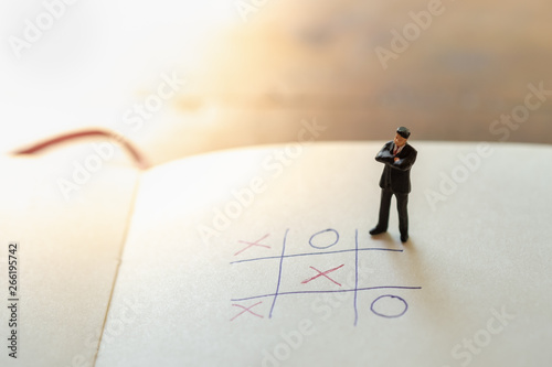 Business direction and planning concept. Businessman miniature figure standing and thinking on paper with OX (tic tac toe) board game.