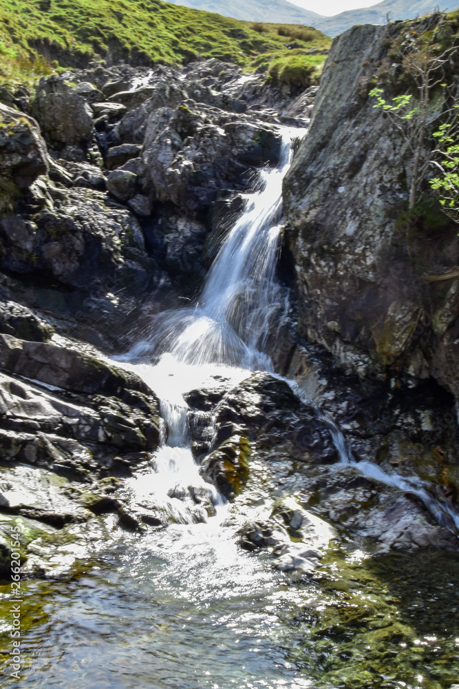 Stream leading out to small waterfall. Slow shutter speed. Bright sunny day. Grisedale pike, Lake District, England, UK