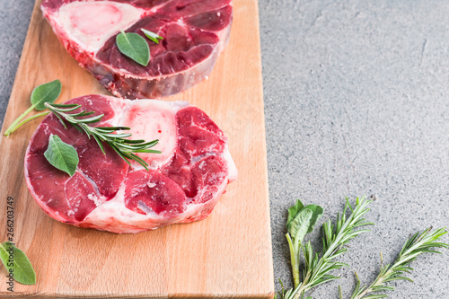 Sliced meat on a wooden board with herbs and spices. Raw meat on the bone close-up. Gray background. Copy space. photo