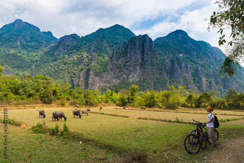 Woman riding mountain bike on dirt road in scenic landscape around Vang Vieng backpacker travel destination in Laos Asia rock pinnacles green valley photo