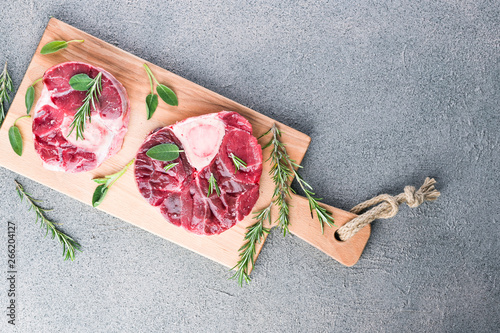 Sliced meat on a wooden board with herbs and spices. Raw meat on the bone close-up. Gray background. photo