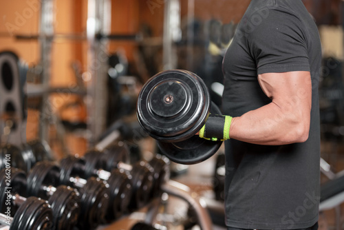 Muscular man working out in gym doing exercises with dumbbells at biceps, strong male .