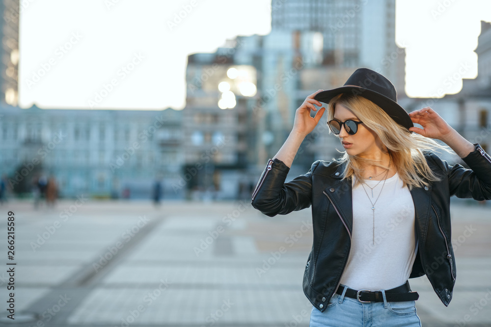 Fototapeta premium Outdoor fashion portrait of a pretty blonde woman wearing hat and mirror sunglasses. Space for text