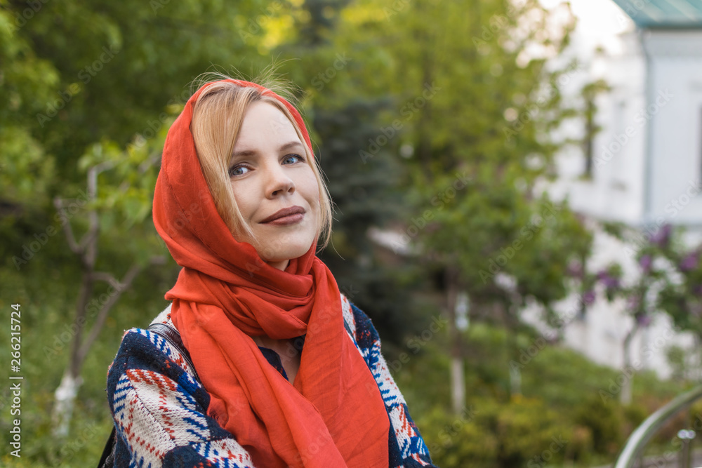 Beautiful middle-aged woman in a red scarf on a background of green trees in the summer. The concept of spring, femininity.