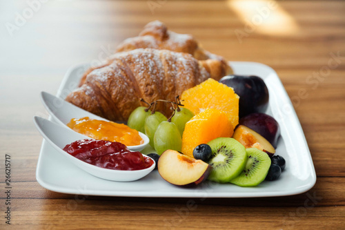 Hotel breakfast plate with assortment of fresh fruit, jam and croissant.
