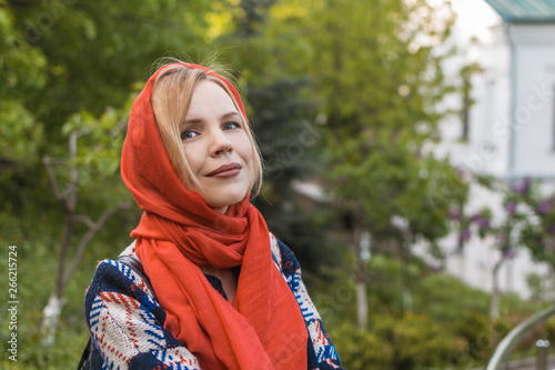 Beautiful middle-aged woman in a red scarf on a background of green trees in the summer. The concept of spring, femininity. © Konstiantyn Zapylaie