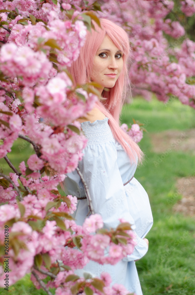 Beautiful pregnant woman with her hands over tummy in blue dress with pink flowers on background