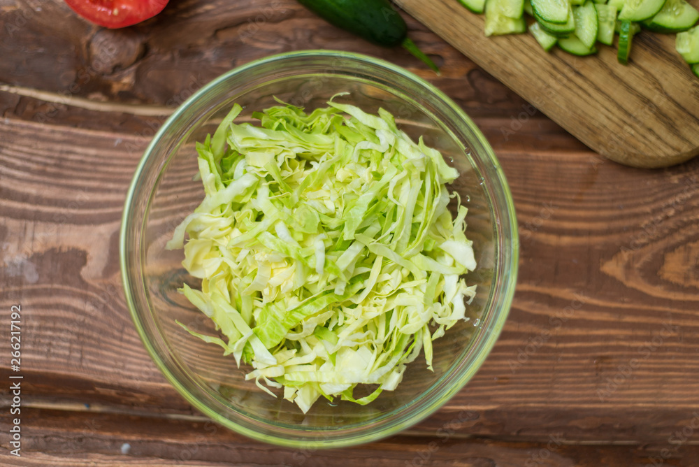 Chopped fresh green cabbage in a glass bowl on a wooden background. Cooking healthy, healthy, vegetable salad. Chopped fresh green cabbage in a glass bowl on a wooden background. Cooking healthy, healthy, vegetable salad.