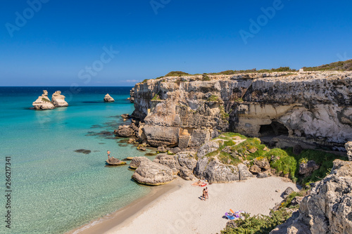 The bay of Torre dell'Orso, with its high cliffs, in Salento, Puglia, Italy. Turquoise sea and blue sky. A beach of fine white and pink sand. The stacks called the Two Sisters. Tourists sunbathe.