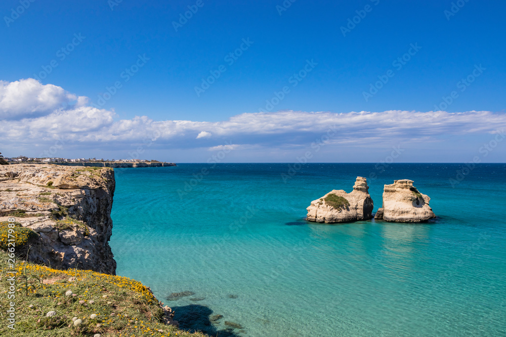 The bay of Torre dell'Orso, with its high cliffs, in Salento, Puglia, Italy. Turquoise sea and blue sky. Panorama of the sea on the horizon and houses on the reef. The stacks called the Two Sisters.