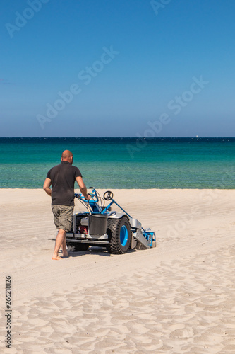 The bay of Torre dell'Orso, with its high cliffs, in Salento, Puglia, Italy. Turquoise sea and blue sky, sunny day in summer. In a bathhouse, a man cleans the sand with a small tractor (sand cleaner).