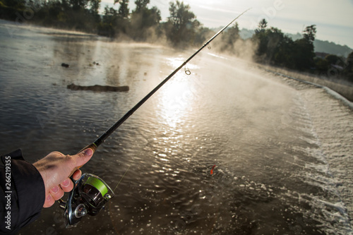 Man fishing in river with fly rod during summer morning.