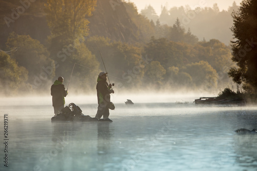 Obraz na plátne Men fishing in river with fly rod during summer morning.