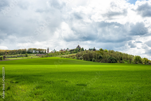 Fototapeta Naklejka Na Ścianę i Meble -  Eye-catching landscape with green grass, trees and monastery up the hill under cloudy sky