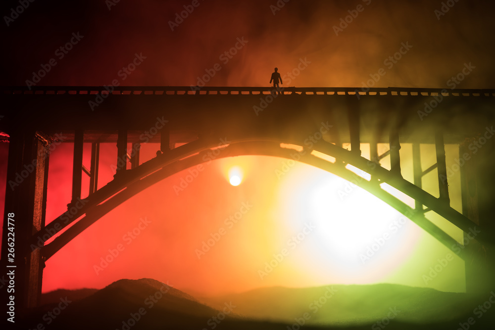 Obraz premium Artwork decoration. Silhouette of powerful metallic bridge at night with foggy backlight. Silhouette of person standing on bridge.