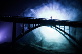 Artwork decoration. Silhouette of powerful metallic bridge at night with foggy backlight. Silhouette of person standing on bridge.