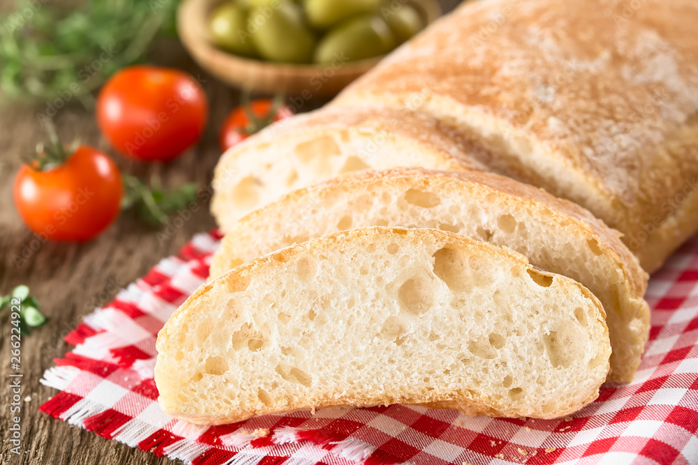 Frisches italienisches Ciabbata Brot in Scheiben geschnitten, Kirschtomaten und grünen Oliven im Hintergrund (Selektiver Fokus, Fokus auf die erste Brotscheibe)