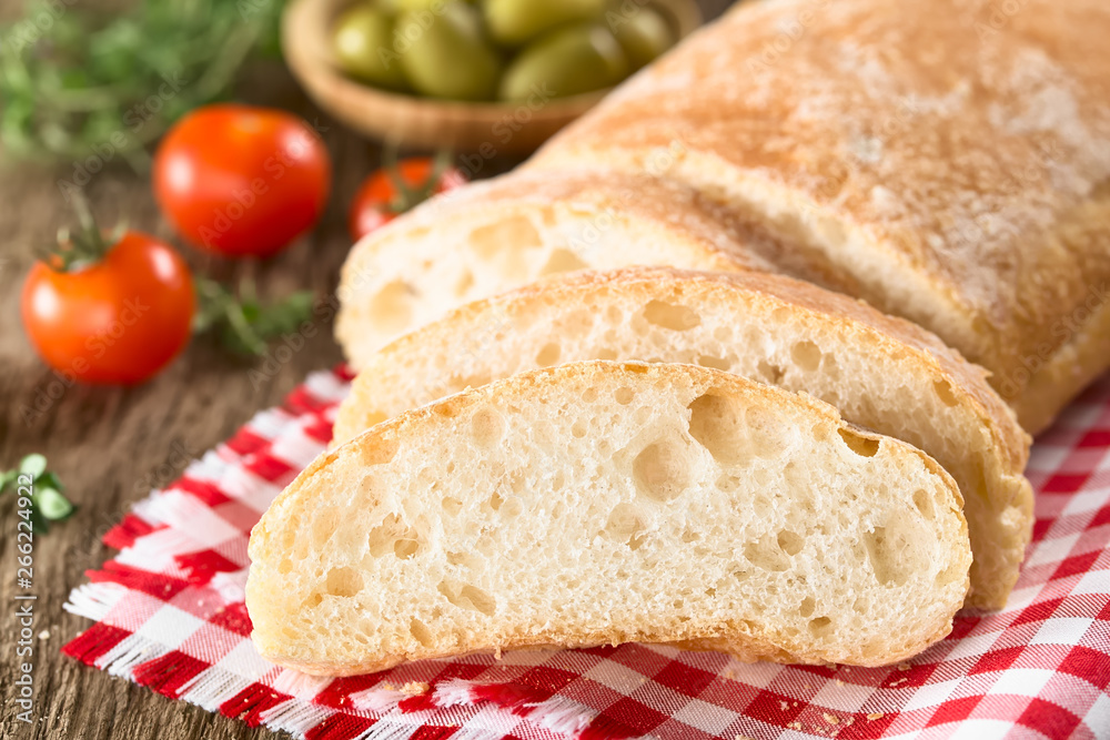 Frisches italienisches Ciabbata Brot in Scheiben geschnitten, Kirschtomaten und grünen Oliven im Hintergrund (Selektiver Fokus, Fokus auf die erste Brotscheibe) Frisches italienisches Ciabbata Brot in Scheiben geschnitten, Kirschtomaten und grünen Oliven im Hintergrund (Selektiver Fokus, Fokus auf die erste Brotscheibe)