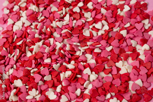 Very small heart-shaped candies are scattered across the background. Many small bright hearts in bulk.
