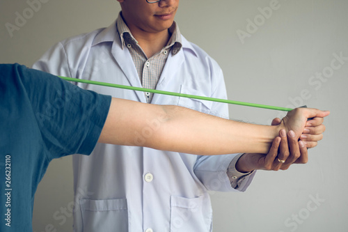 Asian male physical therapist descent working and helping to protect the hands of patients with patient doing stretching exercise with a flexible exercise band in clinic room.