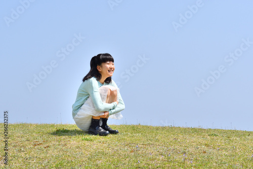 芝生広場に座る女の子（青空） © hanapon1002