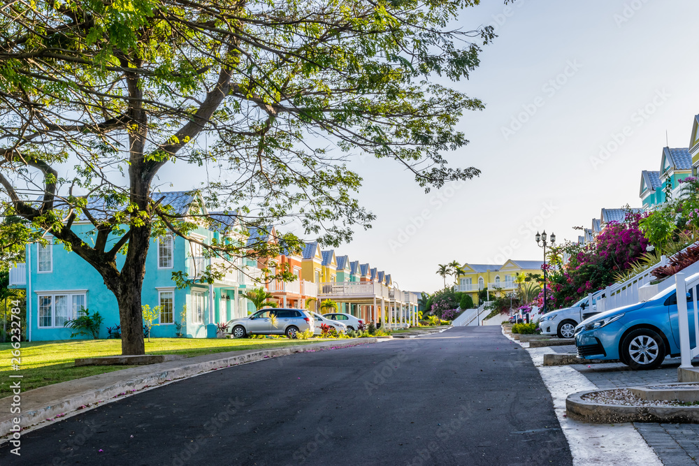 Fototapeta premium Residential neighborhood of colorful town houses/vacation homes. Upscale gated community residences in Caribbean island with manicured lawns, beautiful flowers and trees.