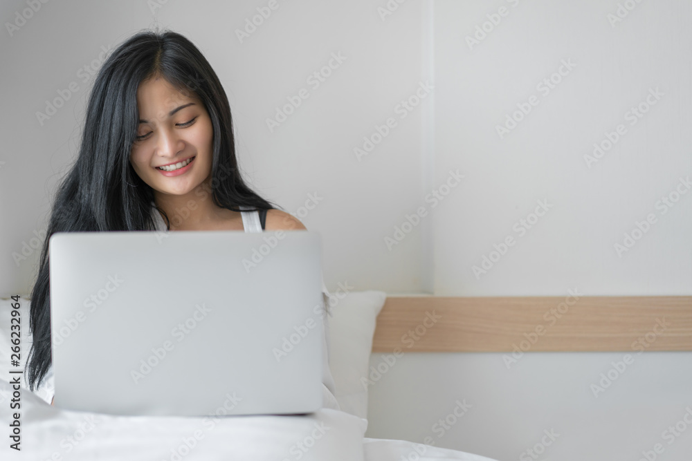 Young woman working on a laptop sitting on bed at home Young woman working on a laptop sitting on bed at home
