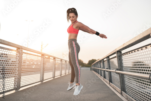 Vitality concept, beautiful young female jumping in the air in sports clothes, sunset 