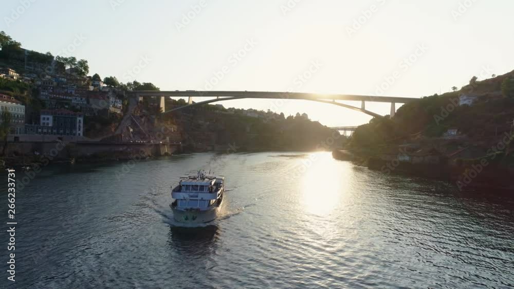 Aerial shot over Douro river, dron flying over cruise boat with tourists floating in sun shining and old european city on banks. Porto, Portugal Aerial shot over Douro river, dron flying over cruise boat with tourists floating in sun shining and old european city on banks. Porto, Portugal