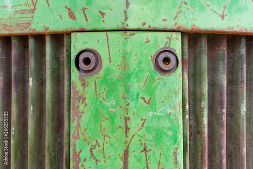 Front nose of farm equipment tractor. Metal background photo with rust, curvy metal vent and green chipping paint.