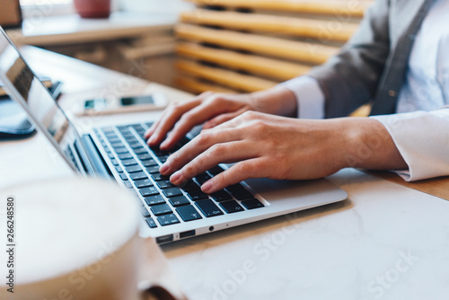 Woman s hands on laptop keyboard texting and typing new ideas and message. Table with cup of coffee in cafe. Close-up